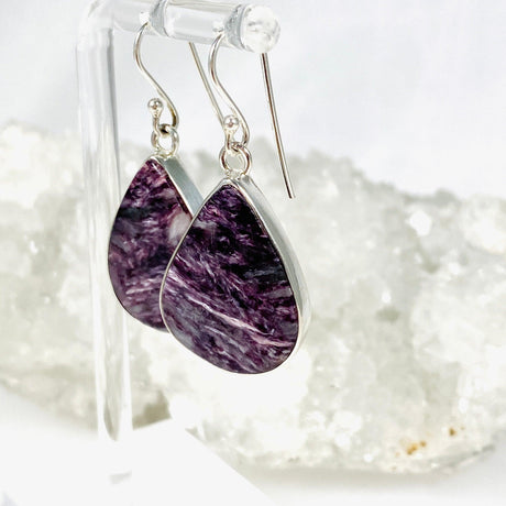 Purple Charoite tear drop earrings in sterling silver hanging on an earring stand