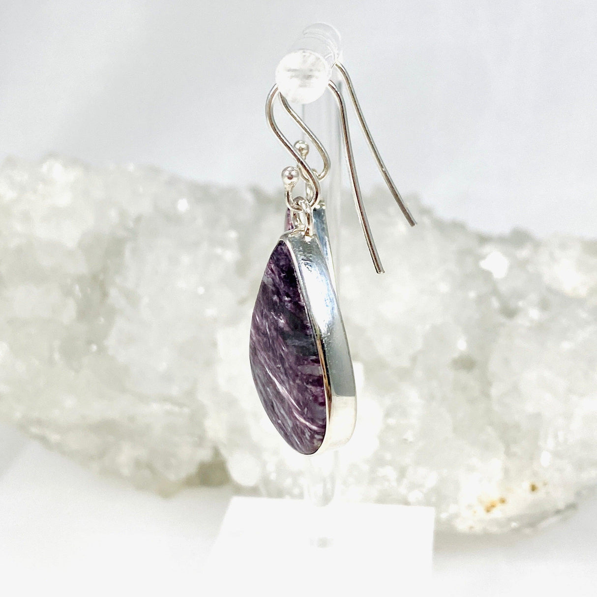 Purple Charoite tear drop earrings in sterling silver hanging on an earring stand
