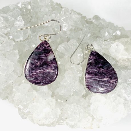 Purple Charoite tear drop earrings in sterling silver sitting on a crystal cluster