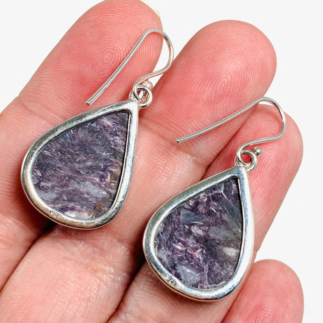 Purple Charoite tear drop earrings in sterling silver sitting in a hand