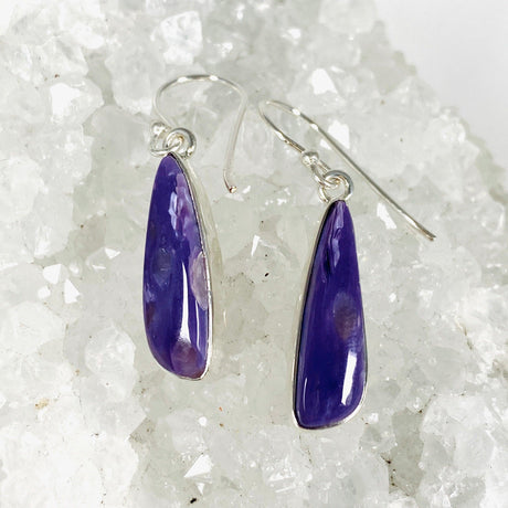 Purple Charoite tear drop earrings in sterling silver sitting on a crystal cluster
