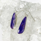 Purple Charoite tear drop earrings in sterling silver sitting on a crystal cluster