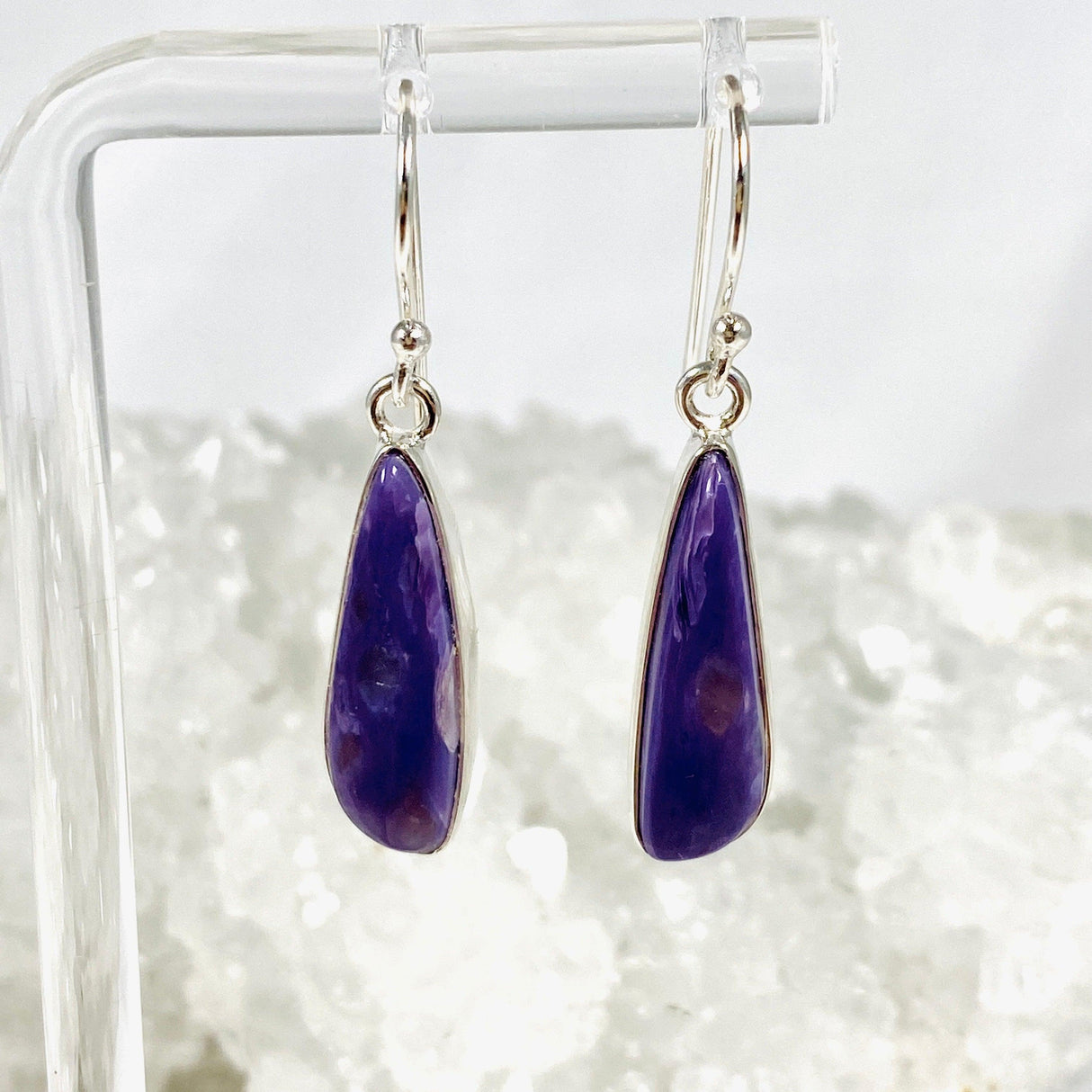 Purple Charoite tear drop earrings in sterling silver hanging on an earring stand