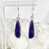 Purple Charoite tear drop earrings in sterling silver hanging on an earring stand