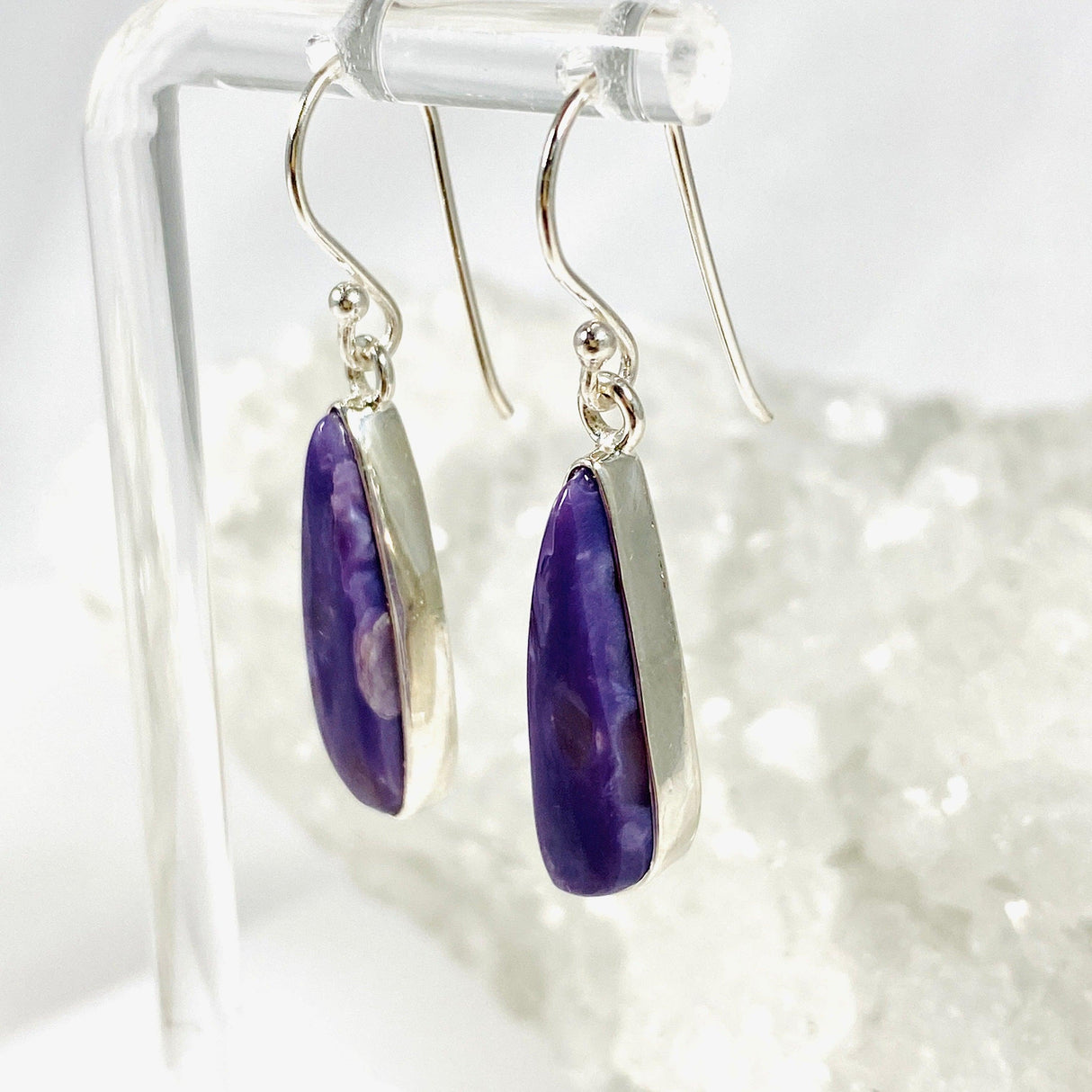 Purple Charoite tear drop earrings in sterling silver hanging on an earring stand