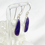 Purple Charoite tear drop earrings in sterling silver hanging on an earring stand