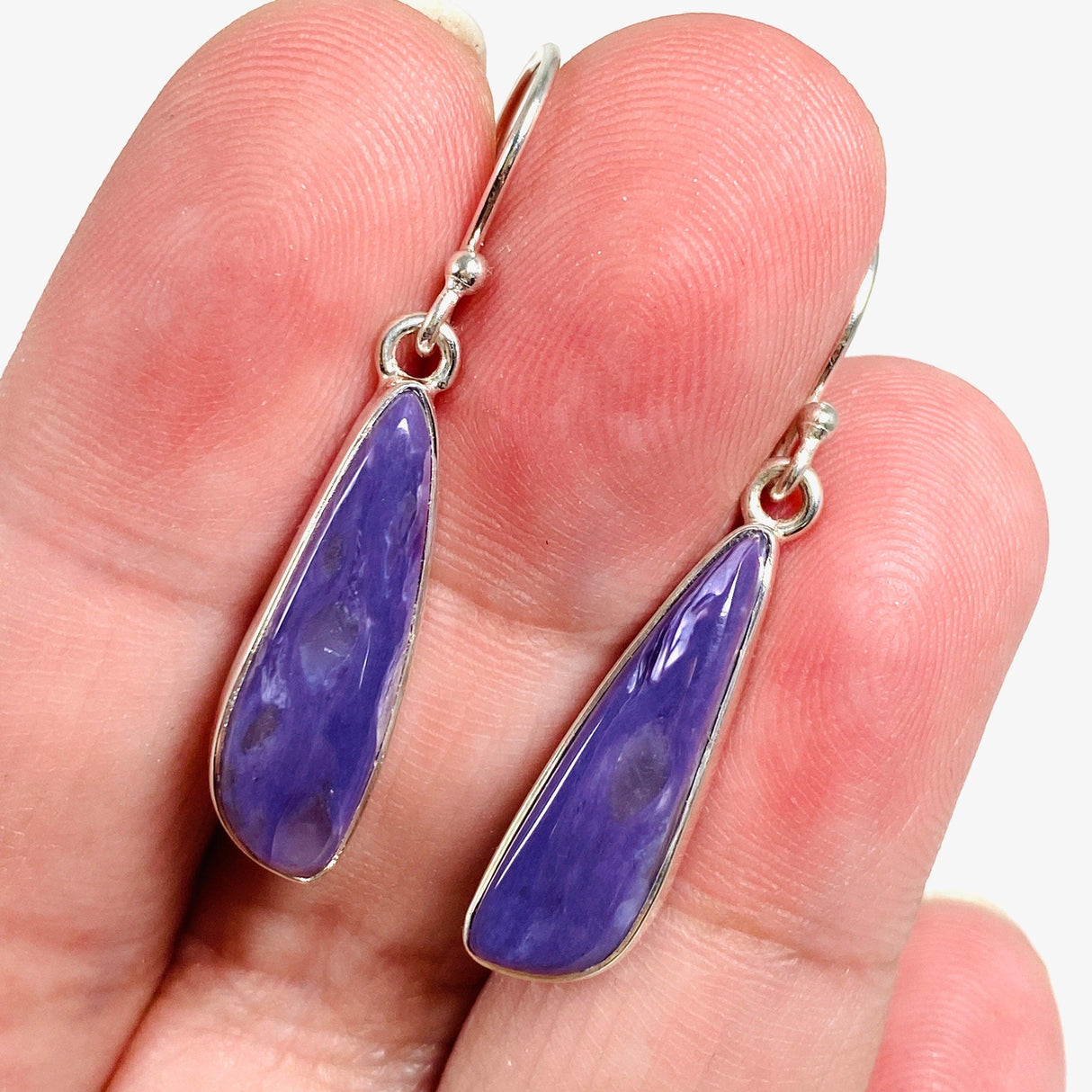 Purple Charoite tear drop earrings in sterling silver sitting in a hand