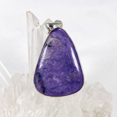 Purple Charoite tear drop pendant in sterling silver sitting on a crystal cluster