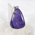 Purple Charoite tear drop pendant in sterling silver sitting on a crystal cluster