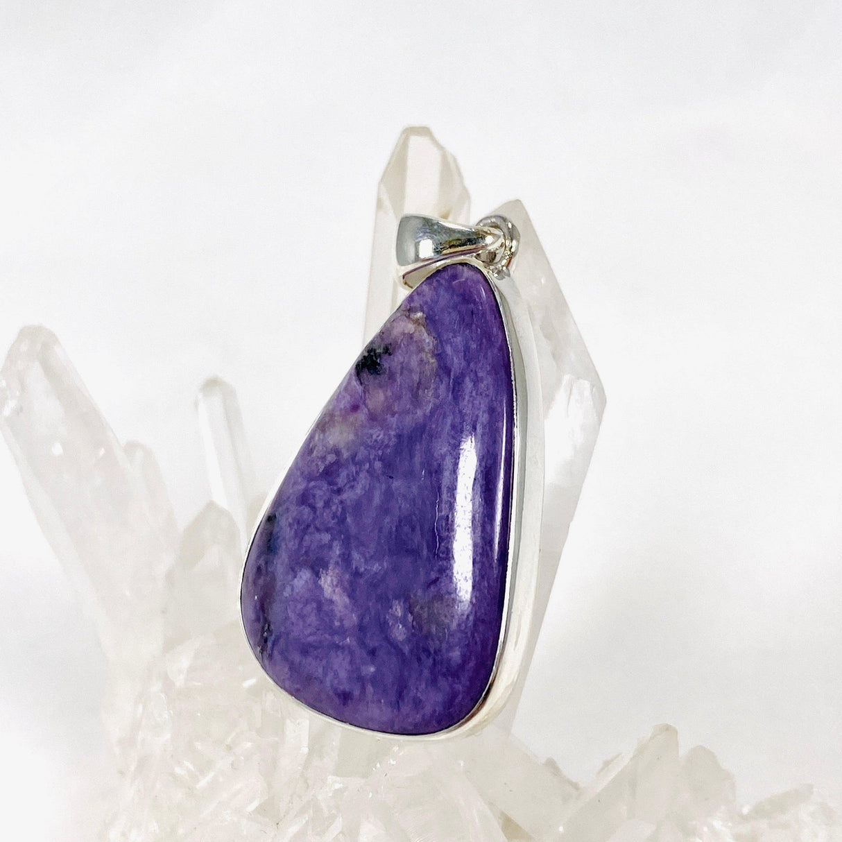 Purple Charoite tear drop pendant in sterling silver sitting on a crystal cluster