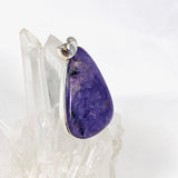 Purple Charoite tear drop pendant in sterling silver sitting on a crystal cluster