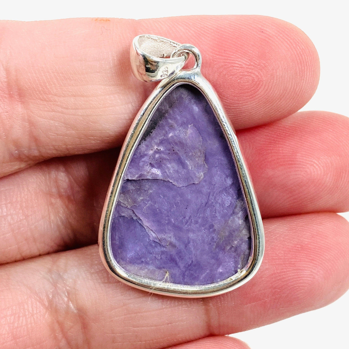 Purple Charoite tear drop pendant in sterling silver sitting in a hand