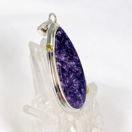 Purple Charoite tear drop pendant with brass detailing  in sterling silver sitting on a crystal cluster