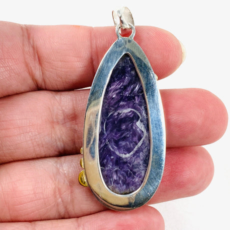 Purple Charoite tear drop pendant with brass detailing  in sterling silver sitting in a hand