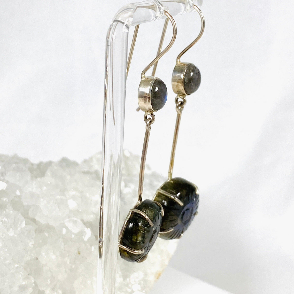 Labradorite and silver earrings with blue flower carving at the bottom with a silver stem going up to a small round labradoite gemstone with a fixed hook hangning from a stand