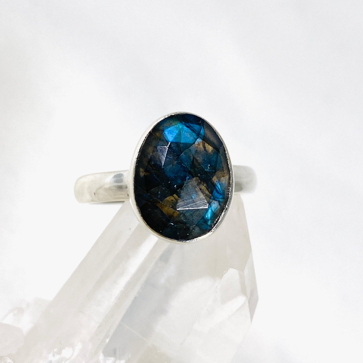 Blue iridescent Labradorite faceted gemstone and silver ring on a clear quartz crystal