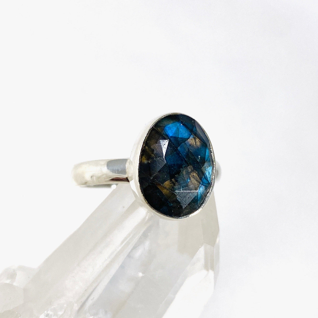 Blue iridescent Labradorite faceted gemstone and silver ring on a clear quartz crystal