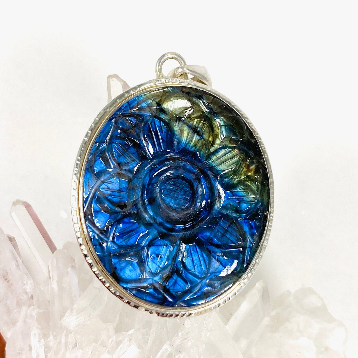 Oval shaped blue and gold flash labradorite flower carving pendant set in silver sitting on a clear quartz crystal