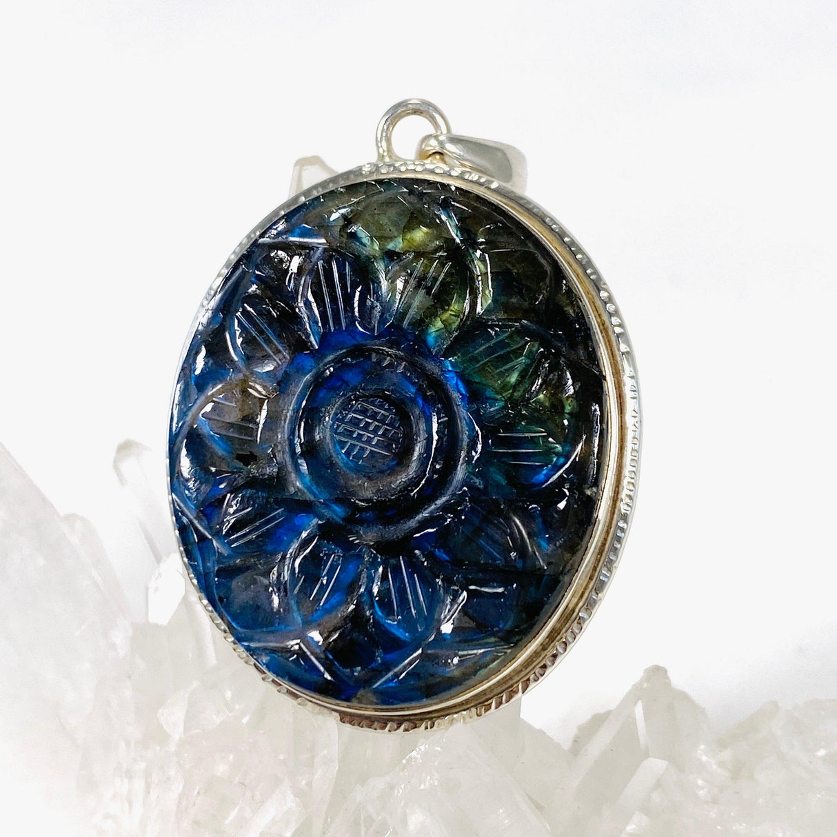Oval shaped blue and gold flash labradorite flower carving pendant set in silver sitting on a clear quartz crystal