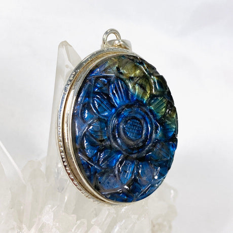 Oval shaped blue and gold flash labradorite flower carving pendant set in silver sitting on a clear quartz crystal