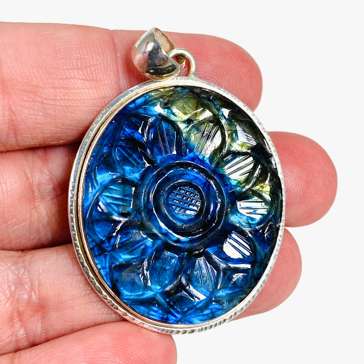 Oval shaped blue and gold flash labradorite flower carving pendant set in silver sitting in the hand