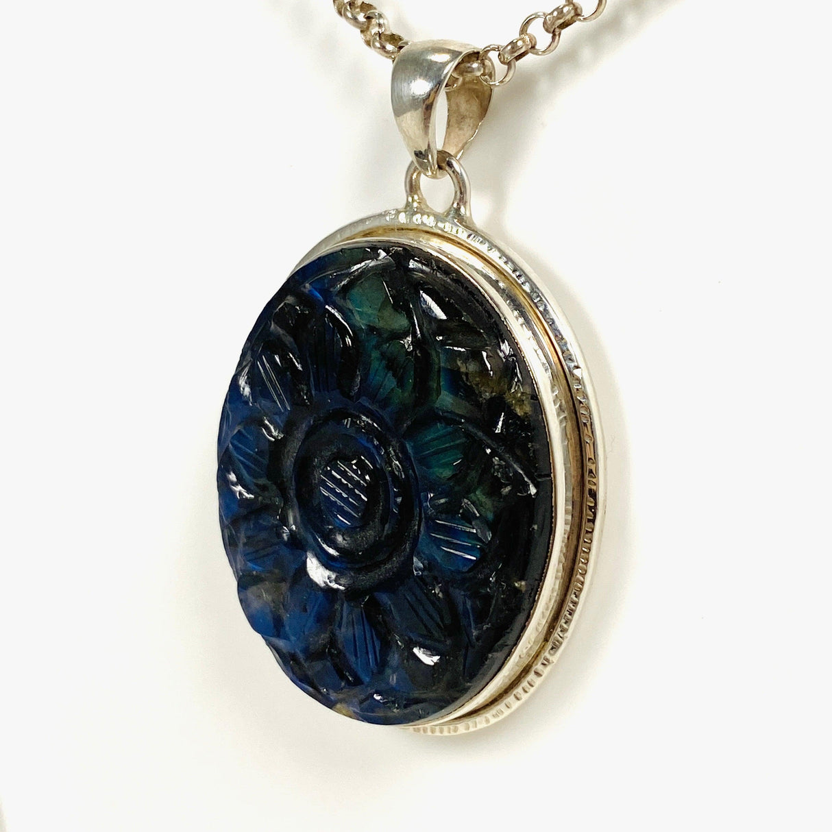 Oval shaped blue and gold flash labradorite flower carving pendant set in silver shown on a silver belcher chain