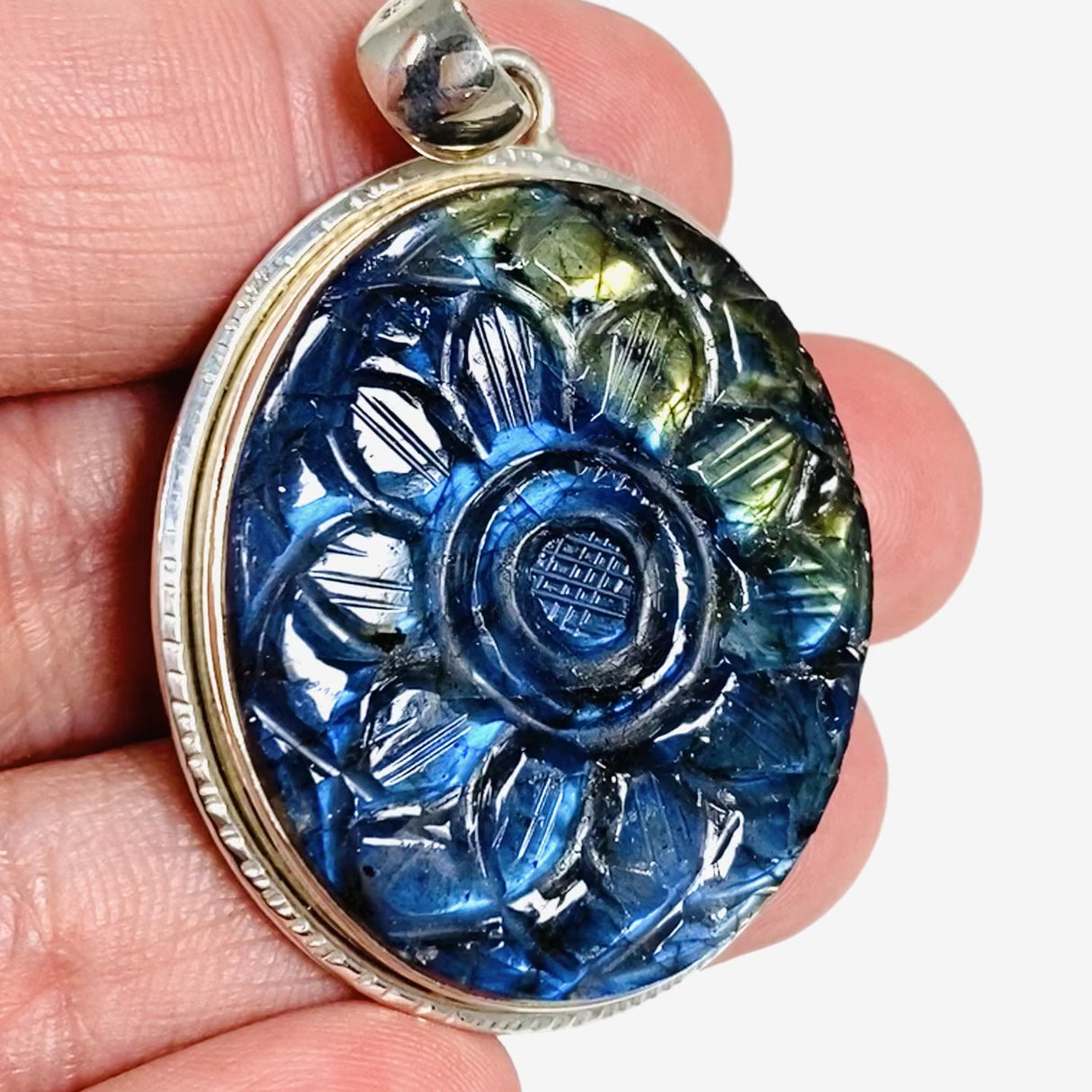Oval shaped blue and gold flash labradorite flower carving pendant set in silver shown in the hand